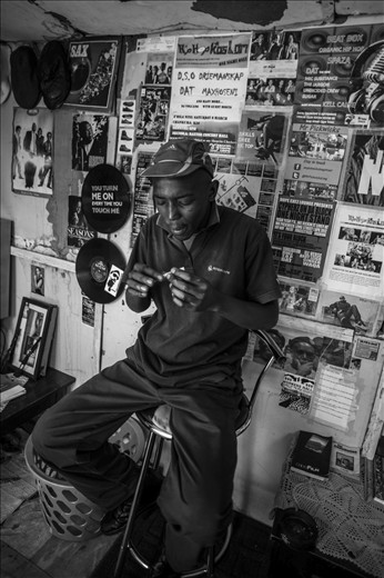 Meet Waqa. Waqa lives in Gugulethu township outside Cape Town, South Africa. After serving time in his late teens for assault, Waqa’s life now revolves around friends, smoking dope, and a passion for hip-hop music known as Spaza, a form of Xhosa township hip-hop he helped to create. Here, he rolls a dakka (marijuana) joint in his backyard shack, his love of Spaza plastered to the walls behind him.