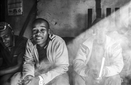 Dakka and Spaza are often found together in the township. Waqa’s friend Lucky (center) runs an outreach group that teaches both locals and tourists about traditional African music—but he also sells marijuana on the side. A shaft of light splits the smoky room. Half revealed and half hidden, part small-time crook and part community musician: like many, Lucky lives on the edge of the law, trying to make a living and still follow his dreams.