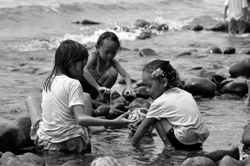 A group of young girls just met on the beach building a pool made of block of stones.
