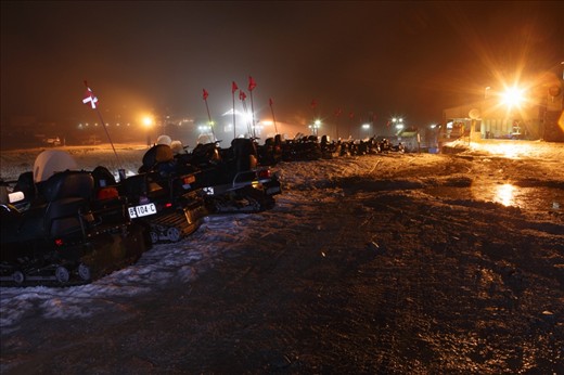 After a long day, Ski Patrol and Mountain Operations Snowmobiles are parked in a row and lit from the loading dock of the main building in Perisher's Front Valley. The main car park can also be seen in the backgound to the left along with the SkiTube terminal in the central background.