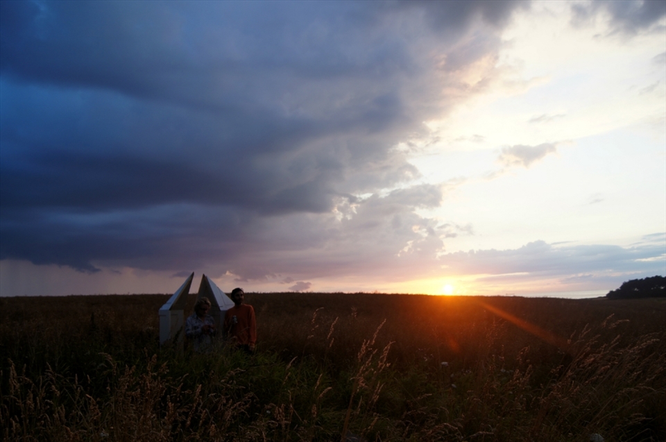 A toast for the sun. Guests in a 'confessional chair' made of old doors. One of numerous art installations around the fields surrounding the farm and festival venue. 