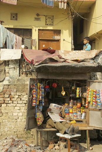 A railway quick stop owner rests with a newspaper, just below his home where his son awaits a train.