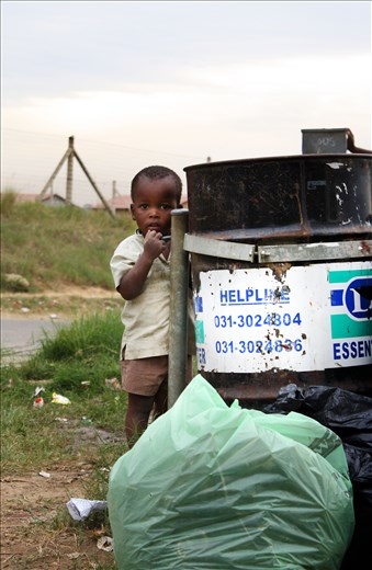 Left to roam the township a young boy watches curiously behind a rubbish bin.