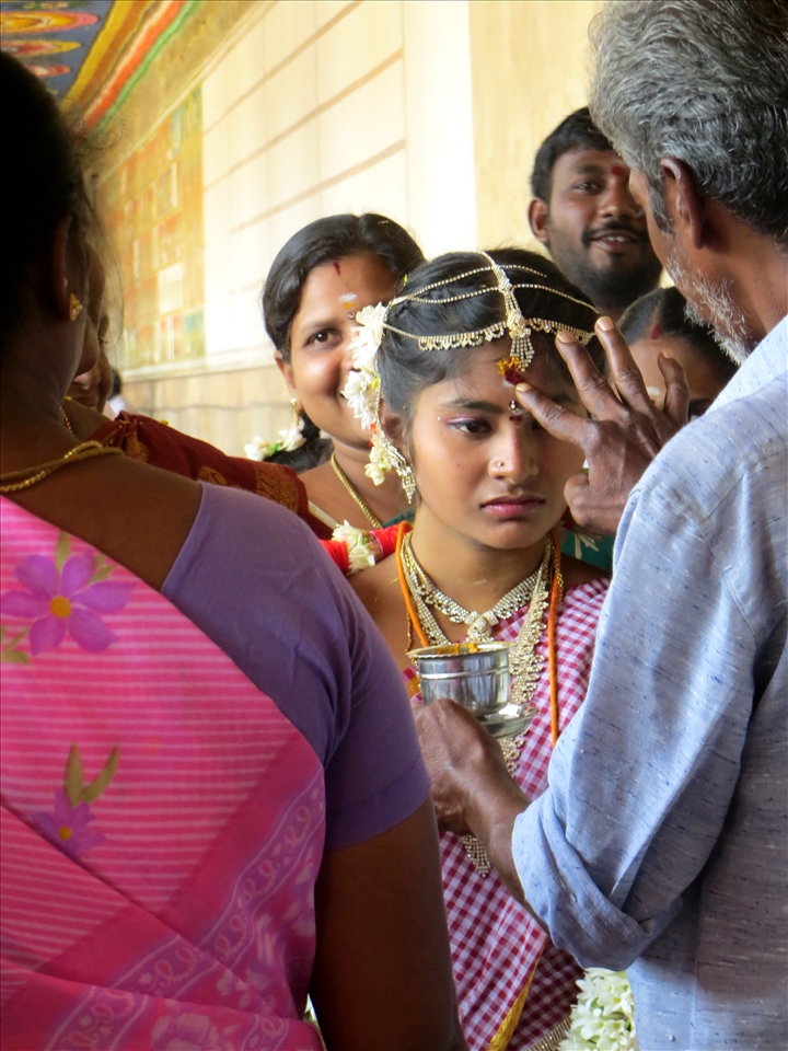 Lost in a sea of smiles on her wedding day, a young bride stares vacantly.