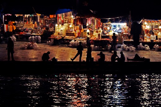 Men whiling away time beside the holy river. On the background are shops selling items of religious significance to the pilgrims.