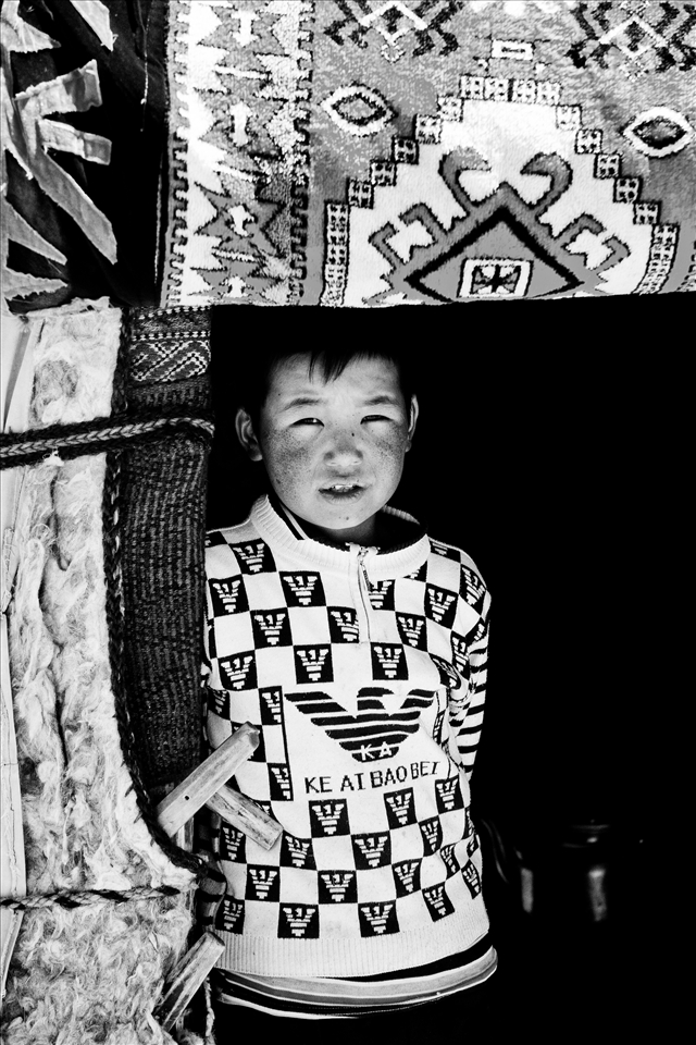 A Kyrgyz boy stands in the doorway of his family's yurt, waiting for visiters. 