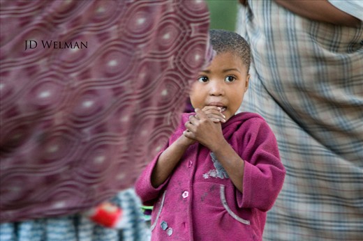 A child stands among a group of dancing women. The women in the tribe dance and engage in traditional games to entertain visiting tourists.