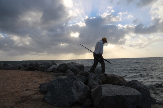 A causal fisherman at work. After the day job, a man is seeing carrying a fishing rod, still lingering on his hobbies with sunset at the background. 