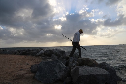 A causal fisherman at work. After the day job, a man is seeing carrying a fishing rod, still lingering on his hobbies with sunset at the background. 