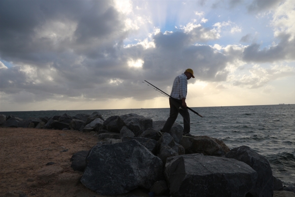A causal fisherman at work. After the day job, a man is seeing carrying a fishing rod, still lingering on his hobbies with sunset at the background. 