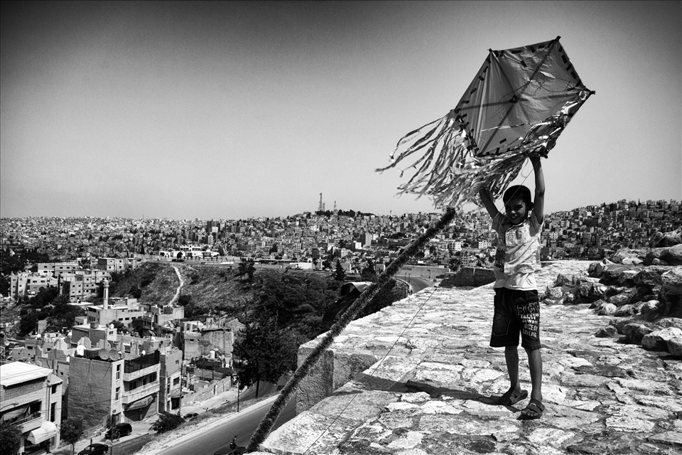 On the citadel walls of downtown Amman, a young boy passes the time playing with a homemade kite. As well as the many minarets that dot the horizon, homemade kites are a common feature of the Ammani skyline; offering a welcome and colorful break to the sprawl of low-rise buildings that cover the city. Amman, Jordan. 