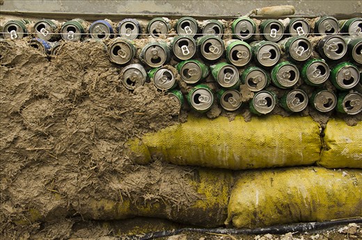 A wall is being built with empty cans of beer, cob and bags full of stones.