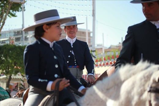 A Sevillan man on horseback travels with his son down the caseta-lined street. Men and women parade the fair grounds on horses and in carriages throughout the day as they travel between casetas, which is where the dancing of sevillanas can be found.