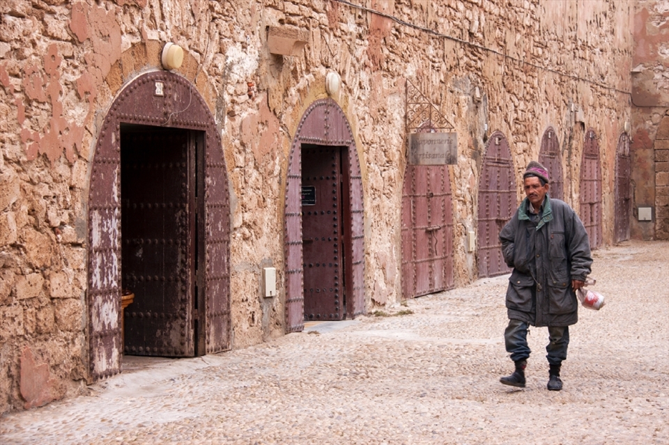 This Moroccan fisherman walks along the street in the Medina quarter (old city section) of the seaside village of Essaouira.  He portrays a solemn figure against the backdrop of monochromatic city walls.