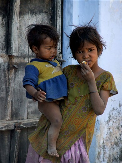 As Jasbir’s family digs a ditch outside her home in Bundi, India, she holds her younger sister as she eats fruit that at any moment will be grabbed out of her hand.