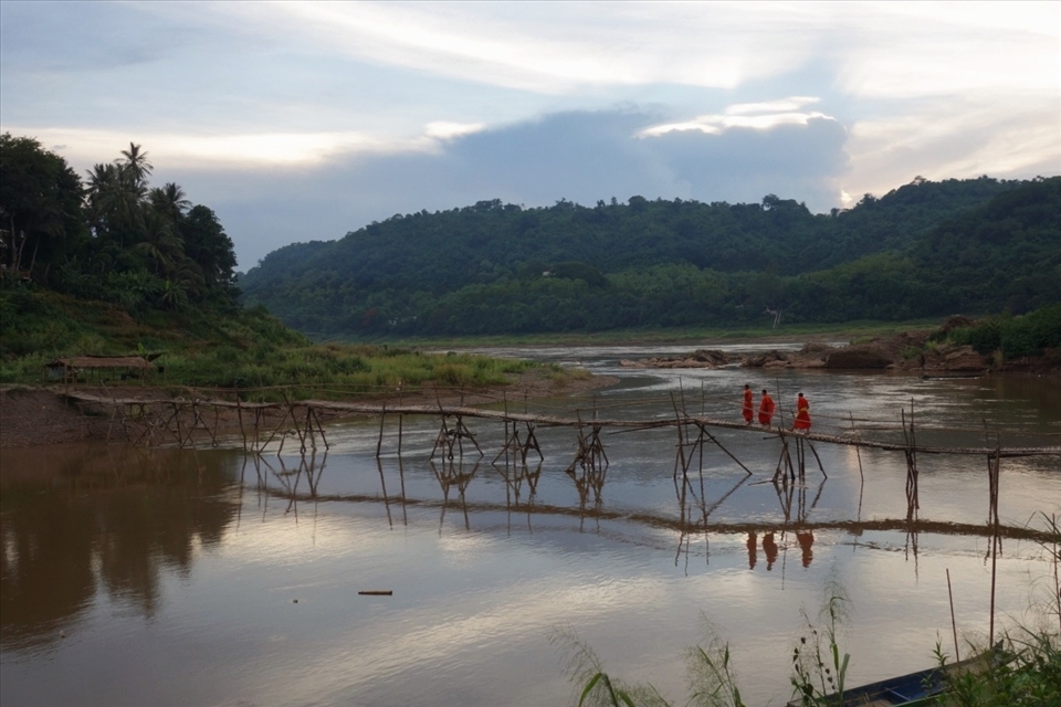 Monks walk across a bamboo bridge over a tributary to the Mekong. 