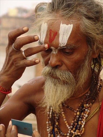 The sadhu prepares for prayer, with the meticulous application of paint markings, or tilakas.