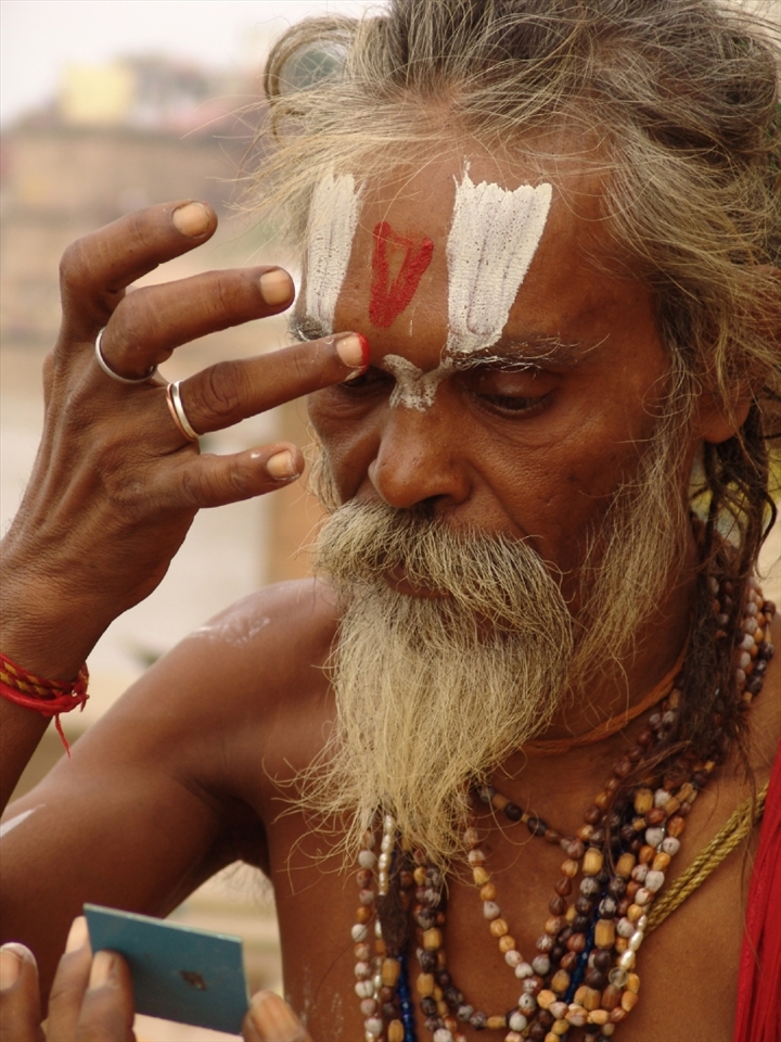 The sadhu prepares for prayer, with the meticulous application of paint markings, or tilakas.
