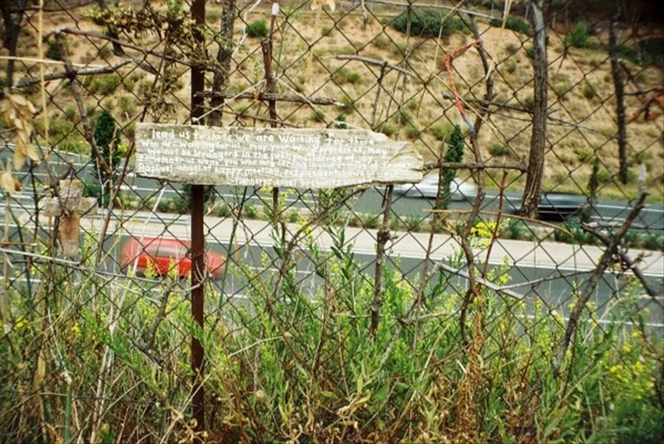 A poem written onto a piece of wood, stuck into the fence near a busy motorway.