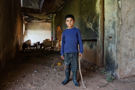 At the age of eleven, this boy, the eldest among his brothers and sisters, is responsible for his family’s small livestock. Since his family lives in an almost deserted house around which the refugee camp is built, he passes through what he considers as “his” old lifeless house and makes use of it as a playground and a pasture to escape the heat of the sun and bring shelter to the cattle. 