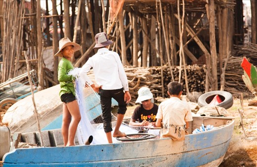 Everyone has their own role to play in the fishing ‘production line’ in the village and here the boys are busy untangling and mending the fishing nets.  In the background the stilt legs of the houses tower above the boat. 