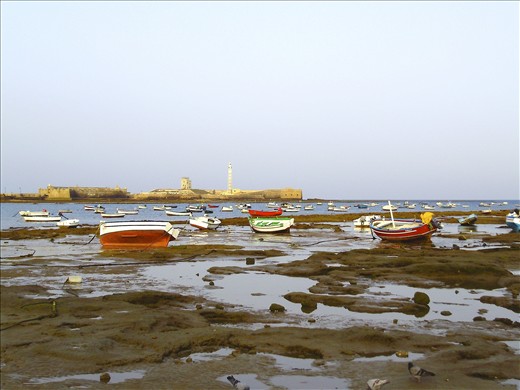 (1) Fishing boats rest on tide flats after sunrise, having already returned with their morning catch. The Castle of San Sebastián, which guided Columbus’ ships out of Cádiz’s harbor on their voyages to America, stands guard in the background.