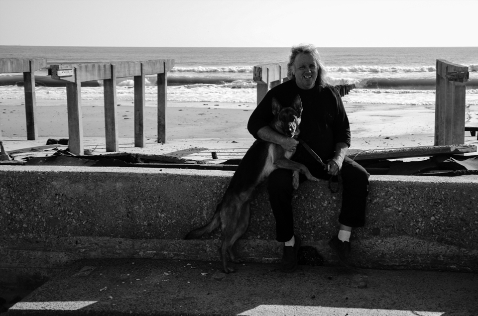 Rockaway Beach, NY: Walking alongside what was left of the boardwalk, I bumped into Tom Ormsby and his protective dog, Roxy. Ormsby lives right by the boardwalk and saw firsthand when the waters rushed in and lifted the boardwalk past his window. When I found him resting by the side of the road with his dog, he was cheerful, but he knew that it would be a while before life in the Rockaways would be restored as he once knew it.. Hurricane Sandy caused an estimated $63 billion USD in damage across the United States on October 2012.