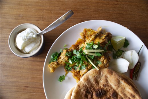Plated karahi with naan and yoghurt.