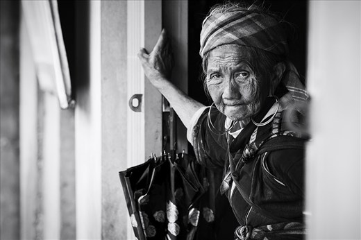 A Hmong Grandmother rests her hands against a door after a long journey through the mountainous region of Sapa. She is carrying her granddaughter in her left arm with the aid of a homemade baby carrier.