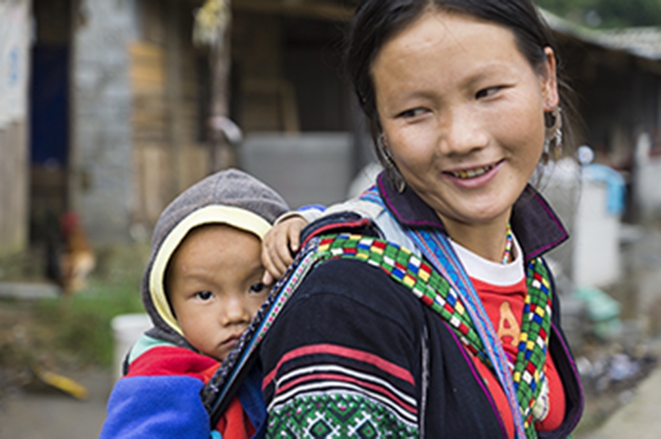 A young mother and son rests and mingles with tourists after a long walk through a local village. Many local Hmong travel and accompany tourists in hopes that they will purchase some of their homemade trinkets/souvenirs.