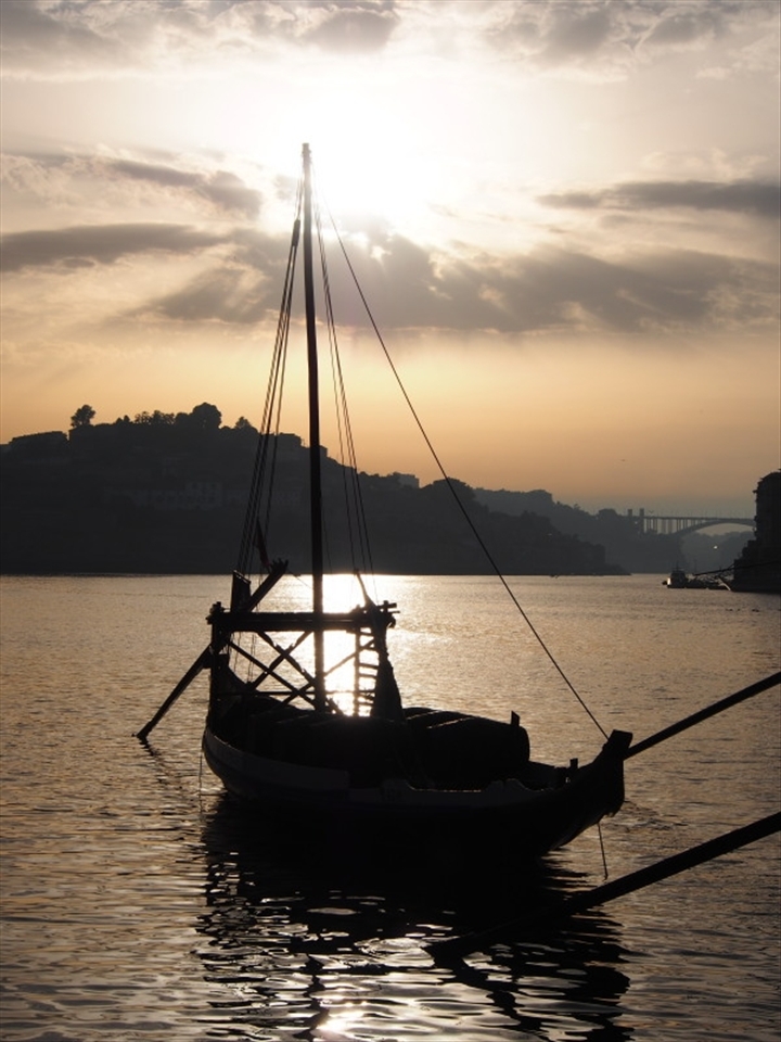 Sun setting on a fading tradition of transportation on the Douro River bathed in golden light giving strength to its name de-ouro, the river of gold.