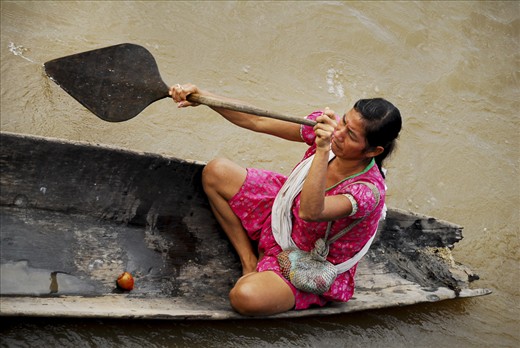 Small dugout canoes are the most common way to get around for people living in Peru's Amazon River region. Those who can afford it may have a small motor on a long shaft attached to their boats, if not, paddles do the job just fine. This woman carries a bag of orange tucuma, a popular snack of boiled palm tree fruit.