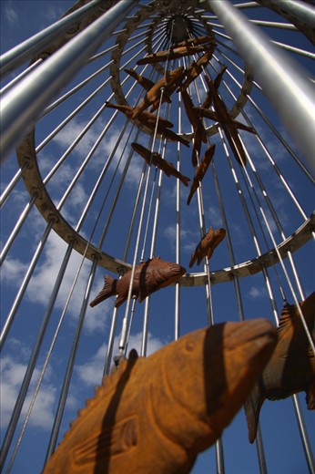 A fishing community. – Monument to reflect.
This community has a long and strong bond with the commercial fishing industry and the Harbour. One of the main tourist attractions is the Harbour walkway, lined with references to the past and present success of the fishing industry in the region.

This monument caught my eye, simplistically reinforcing to visitors the strength of the industry locally.  Not unlike the reality of fish in nets, this monument reflects the daily activity of the region.
