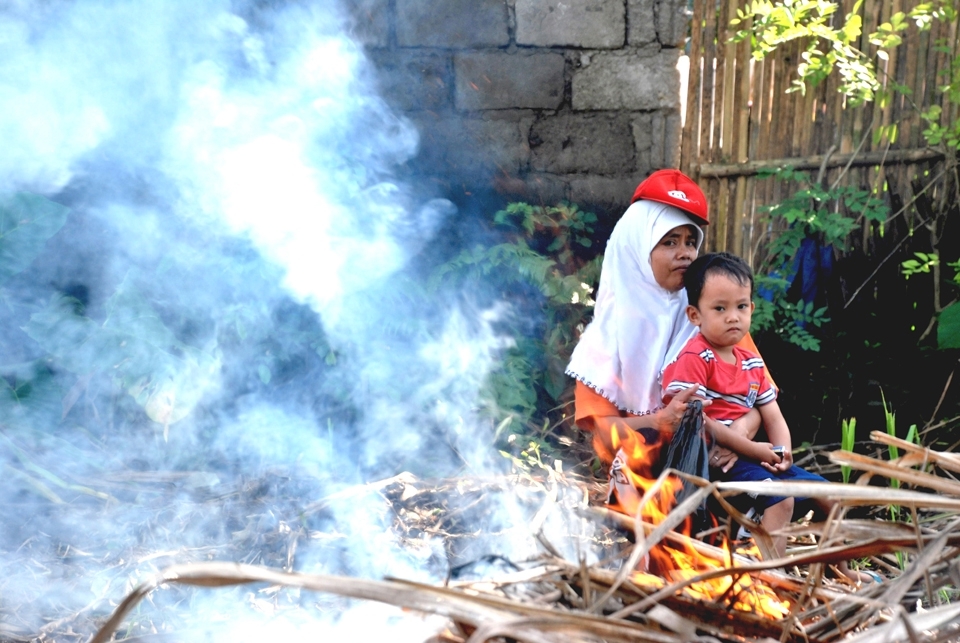 Mrs. Nik and her son, Rofiq, waits in the shades while Mr. Nik works on burning the remaining cane plants after the harvest.