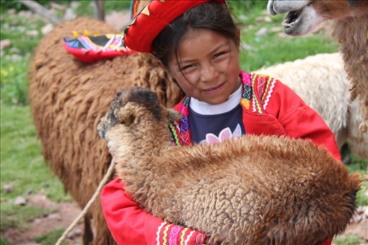 The smile of this little girl is prettier than her colorful clothes and the llama-baby in her arms