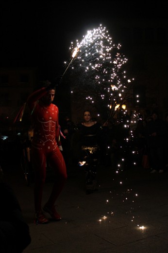 The acrobat and fire thrower alternate between waving batons of sparklers, clearing crowds, and swinging flaming balls of cloth attached to chains.