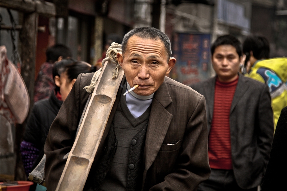 A laborer walks down a busy Zhangjiajie street with his biandan (two baskets and bamboo pole) slung casually over his shoulder and a cigarette dangling effortlessly from the corner of his mouth. 
