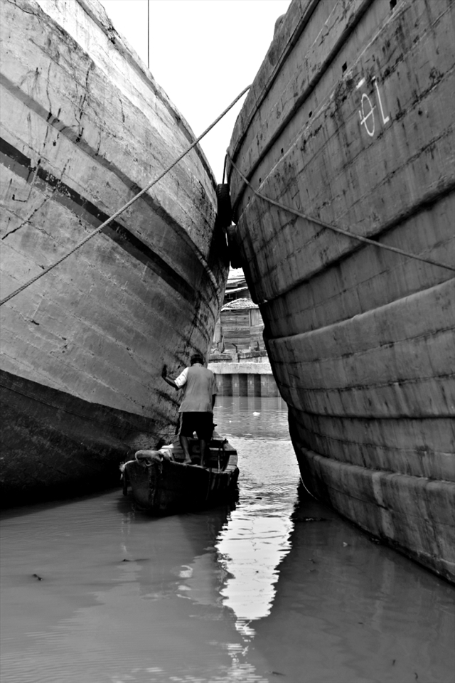 A fisherman paddling between two ship