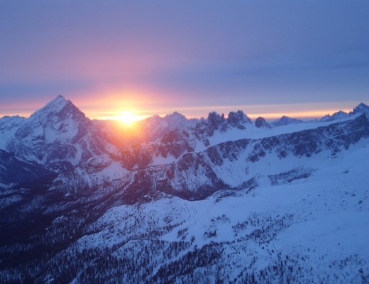 The sun sets, glowing between two peaks of The Dolomites.