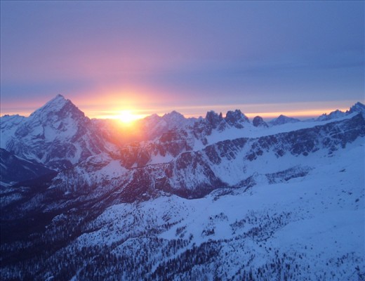The sun sets, glowing between two peaks of the dolomites.