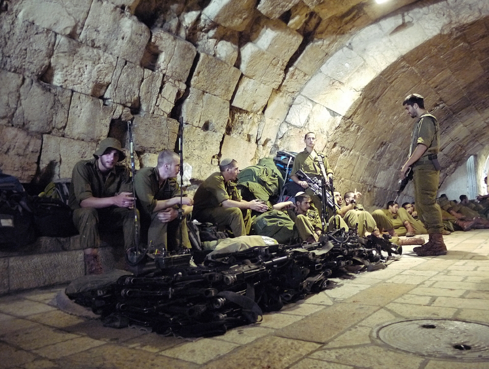 #4 A Moments Rest:  It seemed wherever I was in Jerusalem, I was never far from soldiers. I’d seen a machine gun before, but never a large, neatly stacked pile of them.  I was a little apprehensive about pulling my camera out, but thought I’d regret it if I didn’t. I was given a friendly nod from one of the soldiers, meaning approval was granted, and subsequently took the photo. I think this shot, taken in the old city, accurately reflects the mood and disposition of many of the young, off-duty soldiers I saw. They generally appeared relaxed and chatting, which always made for an interesting juxtaposition when cast against machine guns. There was also a strong sense of comradery between the groups of soldiers I saw, which seems to be typical of young Israelis today. It can be seen not only in the foreground, with the soldier smiling whilst chatting to those seated, but also further back in the shot, where soldiers are all laying down next to each other across their backpacks, limbs intertwined.