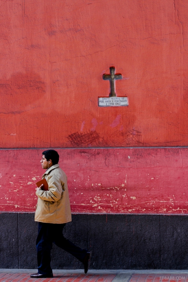 The inscription below this crucifix implores the passerby to venerate this ancient symbol. What is going on in the life of the man who walks by it? Is the book in his hand a bible or a journal? Is he a believer in God? Where is he going, and why does he wear that expression of contentment? What songs play in his ears as he walks the streets of the city? Is it his, or is he one of the many who come to Lima seeking fortune? Despite widespread poverty, pollution and social inequality, the city continues to attract many from the countryside seeking a better life, another passerby in this sprawling metropolis. Another bookcover to a story I'll only have read a line of.

Catholicism, brought by the Spanish Conquistadors, left a deep mark on Peruvian society. The city center of Lima, home to almost a 3rd of Peru's 30 million inhabitants, radiates outwards from the Plaza De Armas, the central square from which all points in Peru are measured. Catholicism played a major role in Peruvian culture and society since conquest and  in some respects it's introduction wiped clean thousands of years of knowledge and belief, leading to the death and persecution of many, and as a justification for the Spanish conquest (
