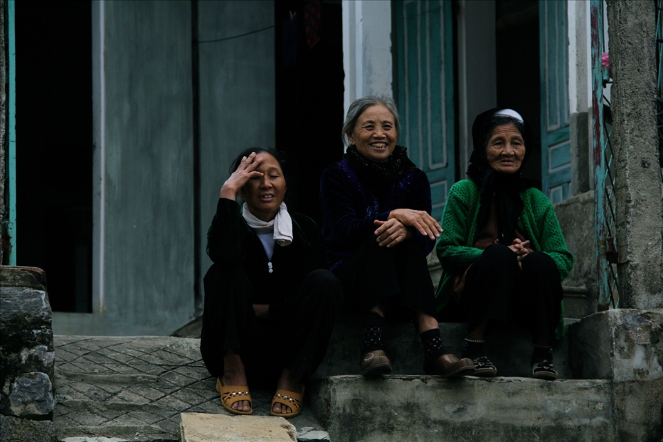 Three women sit talking on a doorstep by the water in the floating village. The small village has great diversity in age, with many elderly people and babies. 