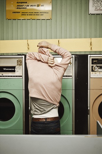 THE AFTERTHOUGHT  A young man removes his jumper to add to his wash. 