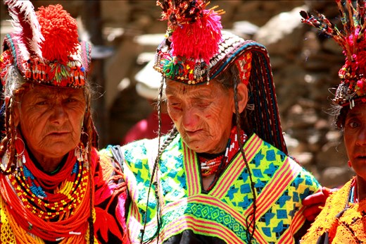 Three Kalasha matriarchs, decked in traditional finery, their faces wizened by the harsh mountain sun and long days of work in the fields, dance arm-in-arm during Joshi festivities. 
<p>
A world apart from the conservative, male-dominated,predominantly Muslim society of Pakistan, the women of Kalash enjoy certain exceptional freedoms. They do not observe <i>purdah</i>, they mix openly with men, and they customarily choose their own husbands, whom they are allowed to divorce at will. The goddess Jestak, protector of home and hearth, holds an important place in the Kalash pantheon, and the four-day spring festival normally kicks off with sacrifices made in her honor. 
