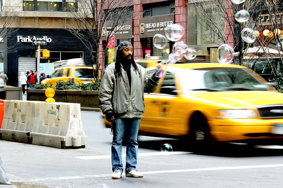 A Jamaican man sells bubble guns in a crossing-road of Midtown. The colorful bubbles clash with the grey of a winter afternoon. 