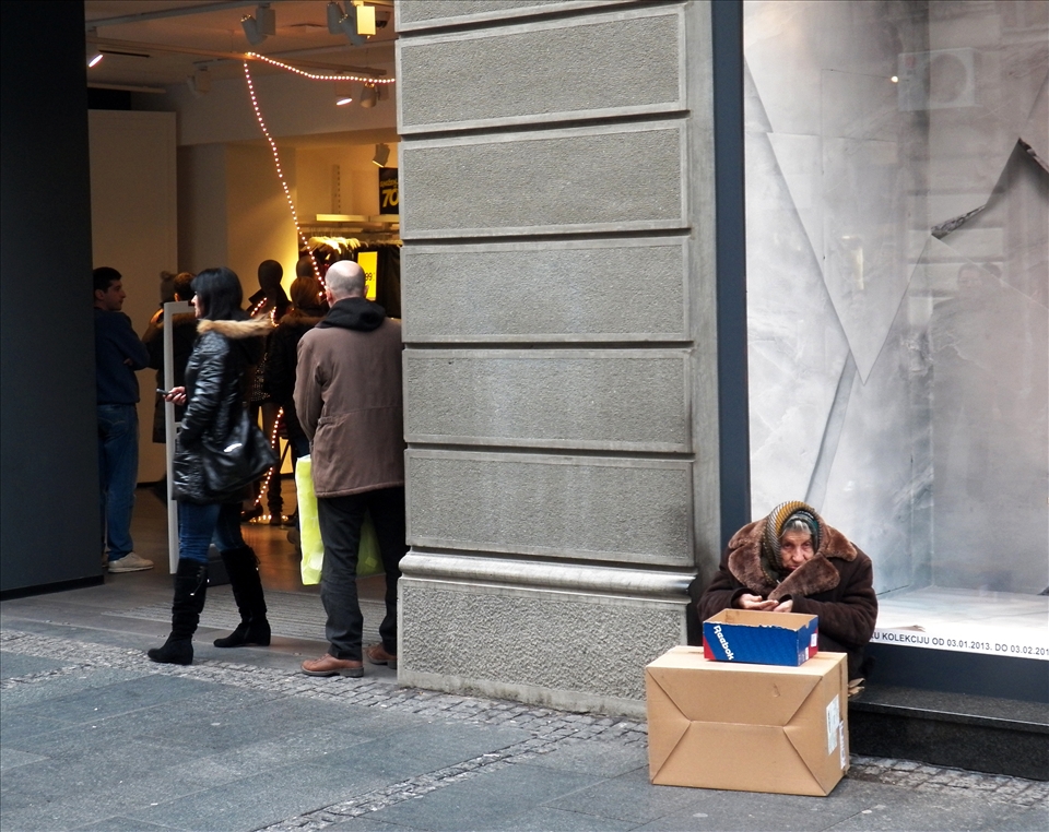 An old woman begging in front of the modern and expensive clothing shop
