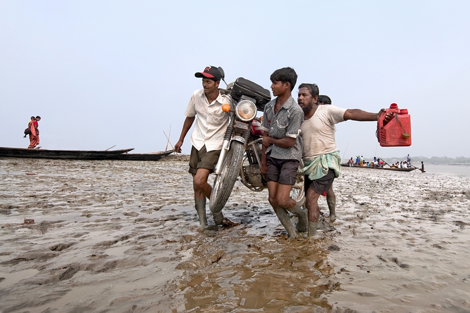 At the Low  time a Bike Owner crossing the Matla River bed with the help of Othe