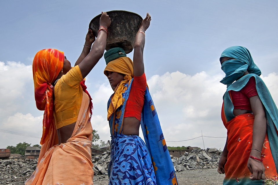 Womens are helping each other to lift up the heavy stone in the bucket