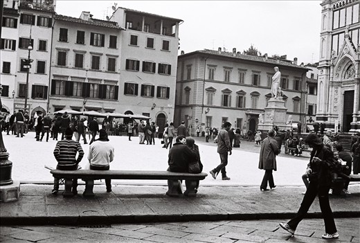 A tourist couple embrace, while soaking up the square’s atmosphere from the comfort of bench. Florence, Italy.